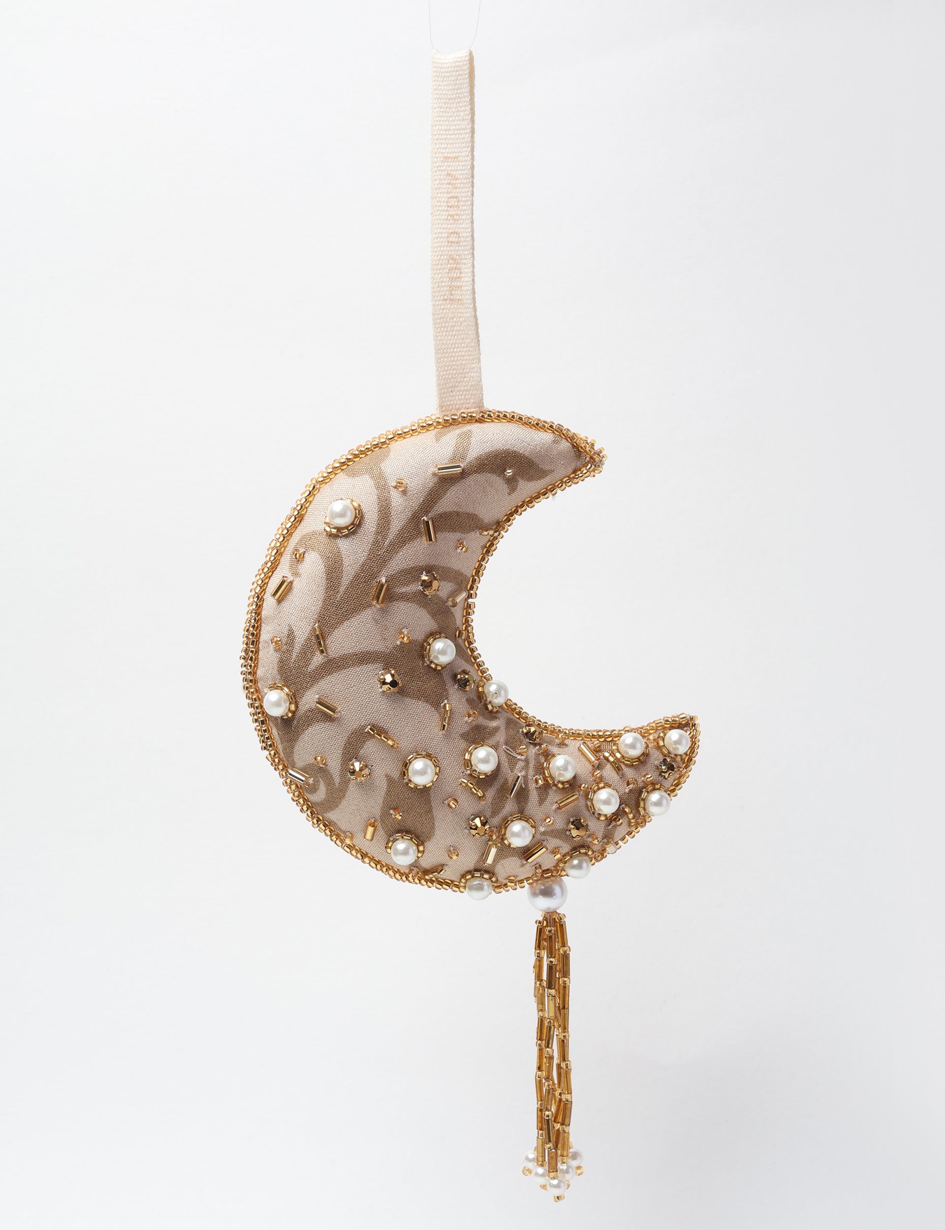 Gold crescent moon ornament with pearl and gold bead embellishments, fabric texture, and hanging tassel detail