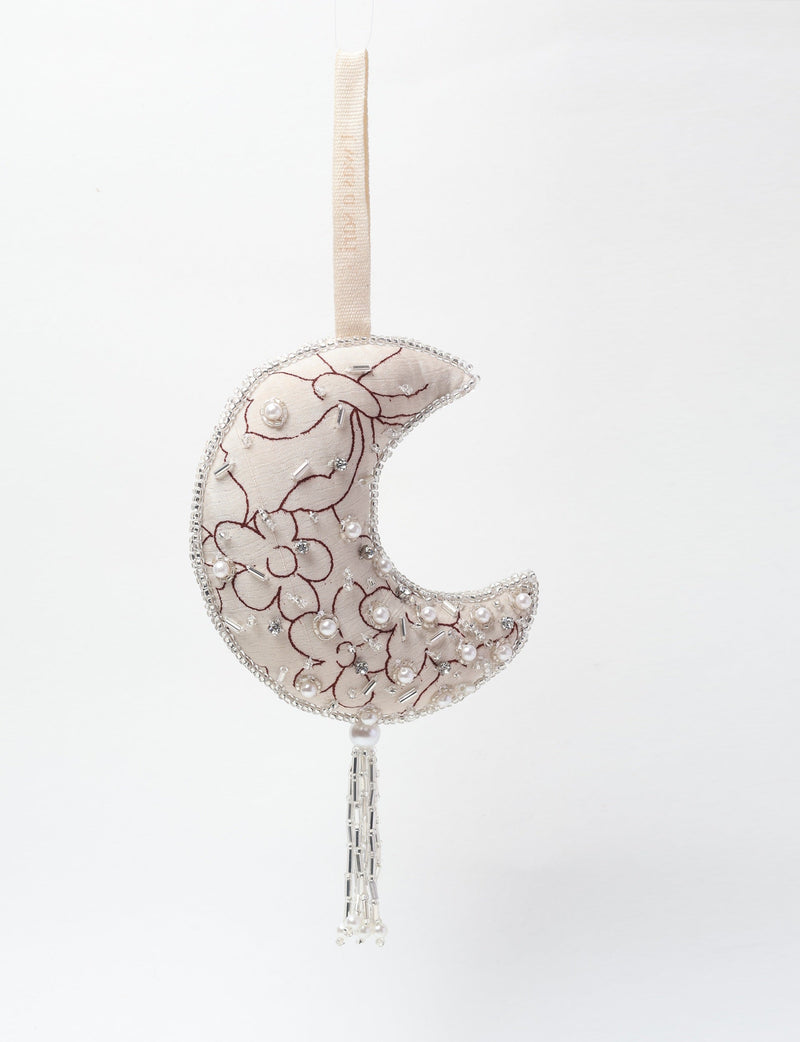 Silver crescent moon ornament with floral embroidery, pearl and bead embellishments, hanging by a fabric loop with tassel fringe