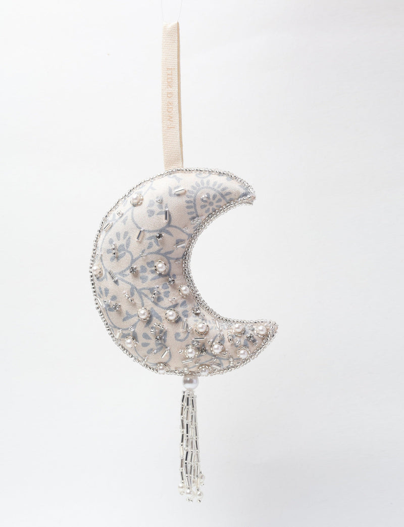 Silver crescent moon ornament with floral pattern, pearl and bead embellishments, hanging tassel, and fabric loop hanger