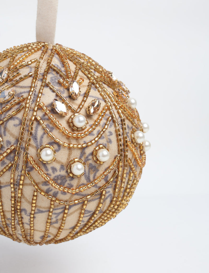 Gold fabric ball ornament with gold beads, clear rhinestones, and pearl embellishments, hanging by beige ribbon loop