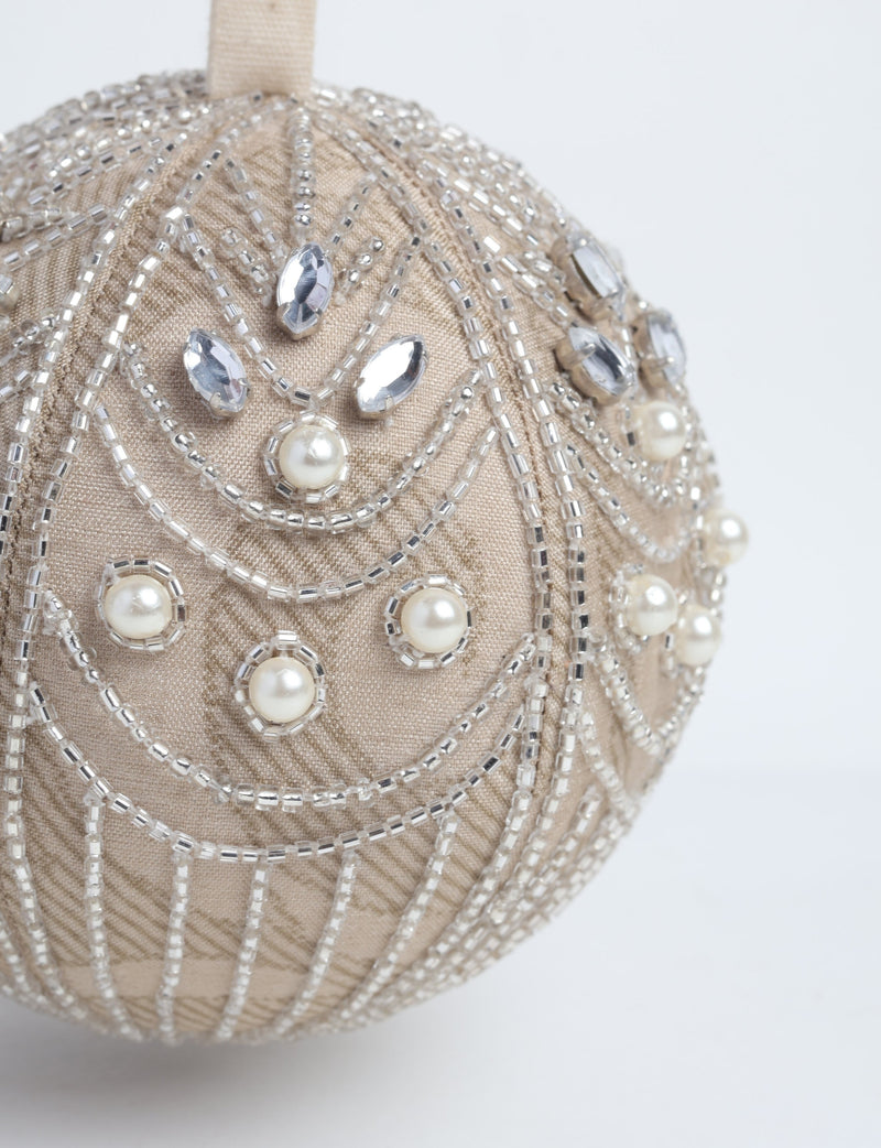 Beige fabric ball ornament decorated with silver beads, clear gems, and pearl-like accents, hanging by a beige loop
