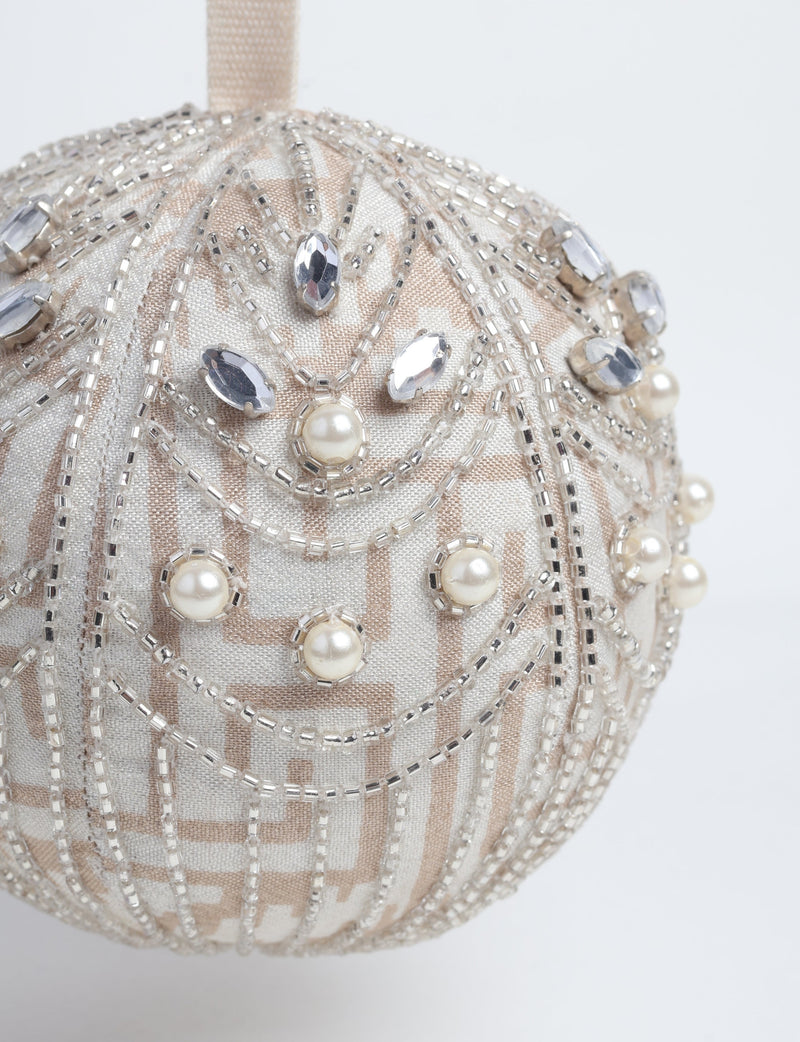 Silver fabric ball ornament with beige geometric pattern, decorated with clear beads, faux pearls, and rhinestones, hanging view