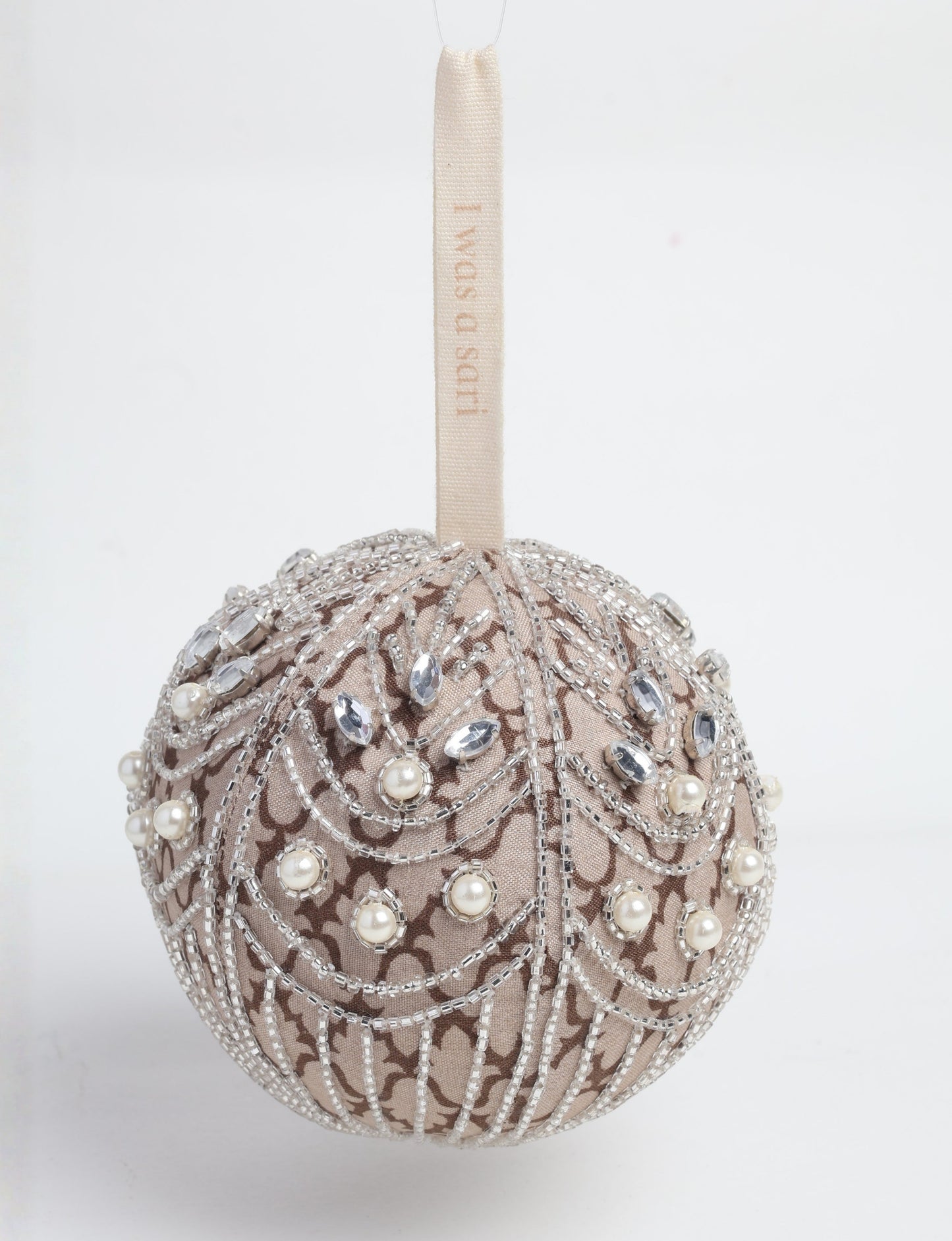 Silver fabric ball ornament with intricate beadwork, pearls, and clear gem embellishments, hanging by a beige loop with text