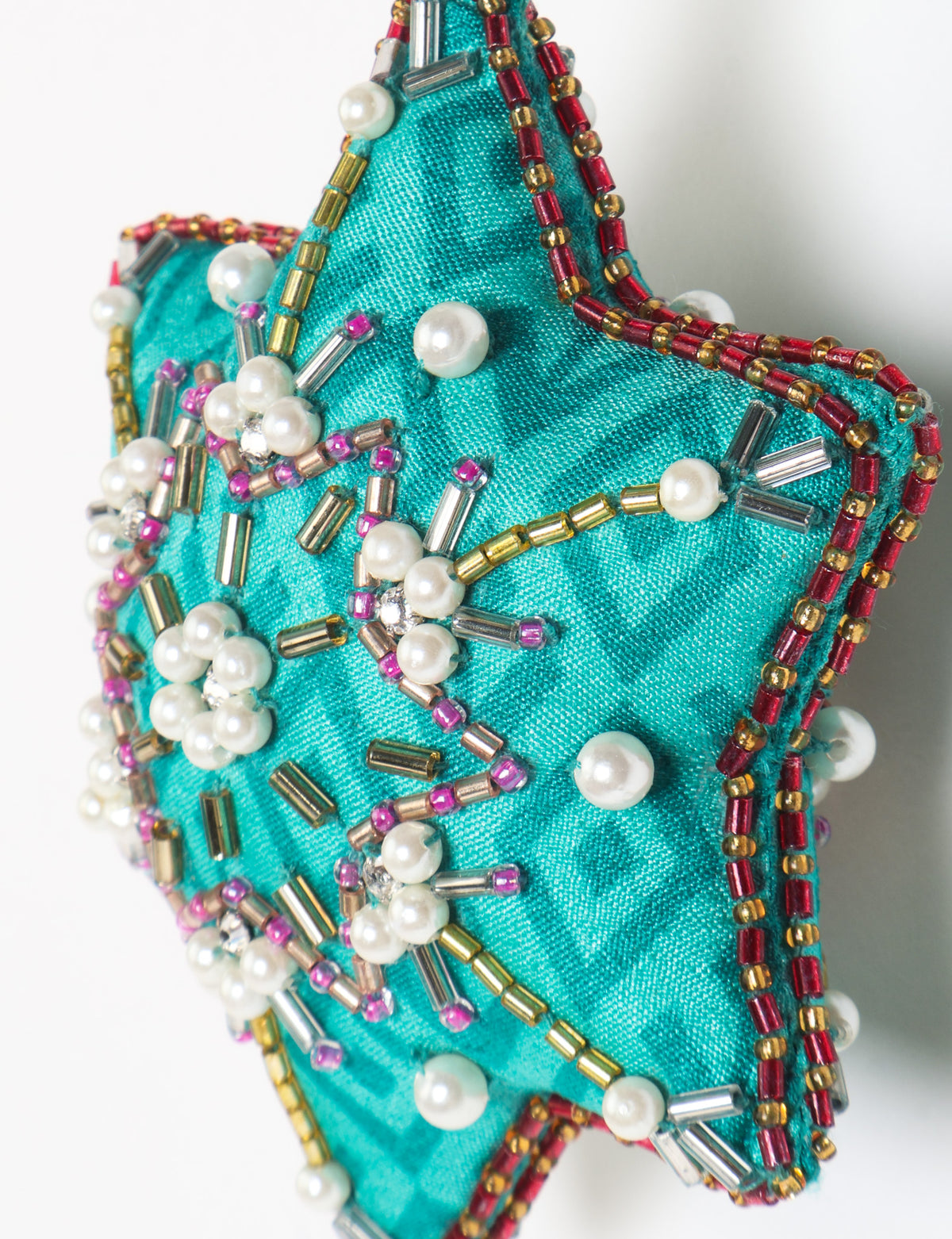 Teal fabric star-shaped snowflake ornament with bead and pearl embellishments, hanging by a teal fabric loop