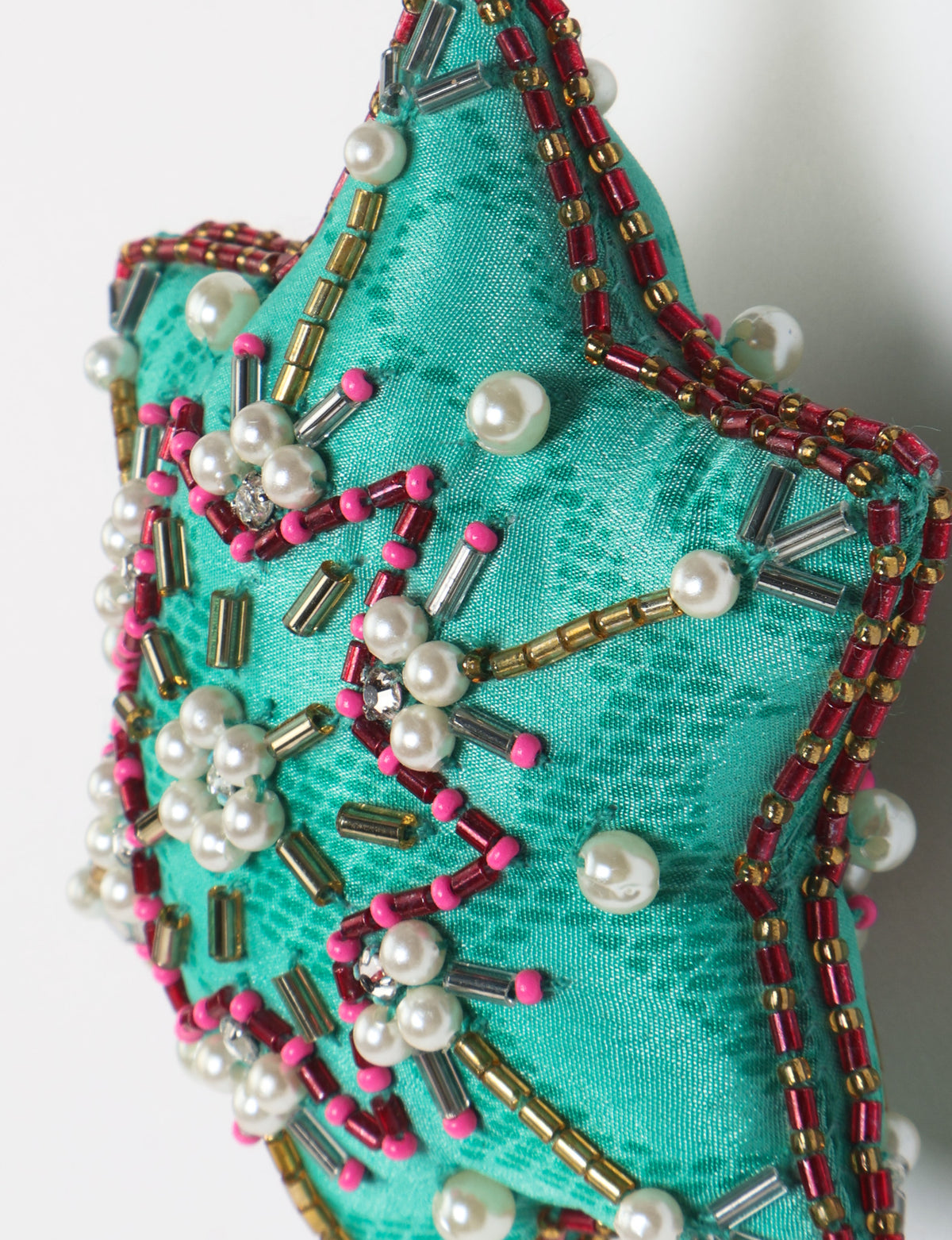 Teal fabric star-shaped snowflake ornament with bead and pearl embellishments, hanging by a teal fabric loop