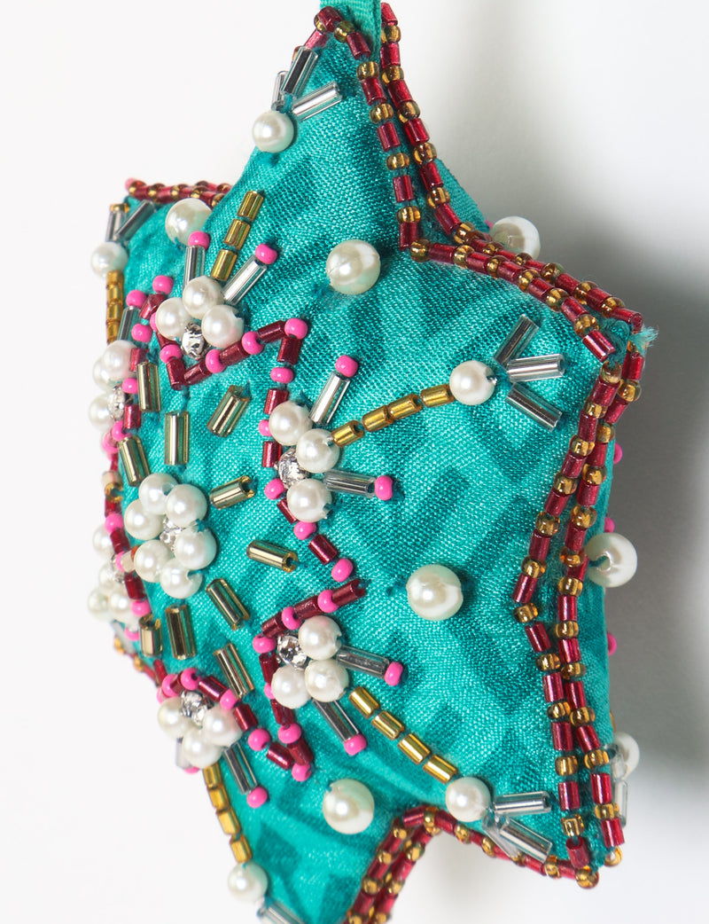 Teal fabric star-shaped snowflake ornament with bead and pearl embellishments, hanging by a teal fabric loop