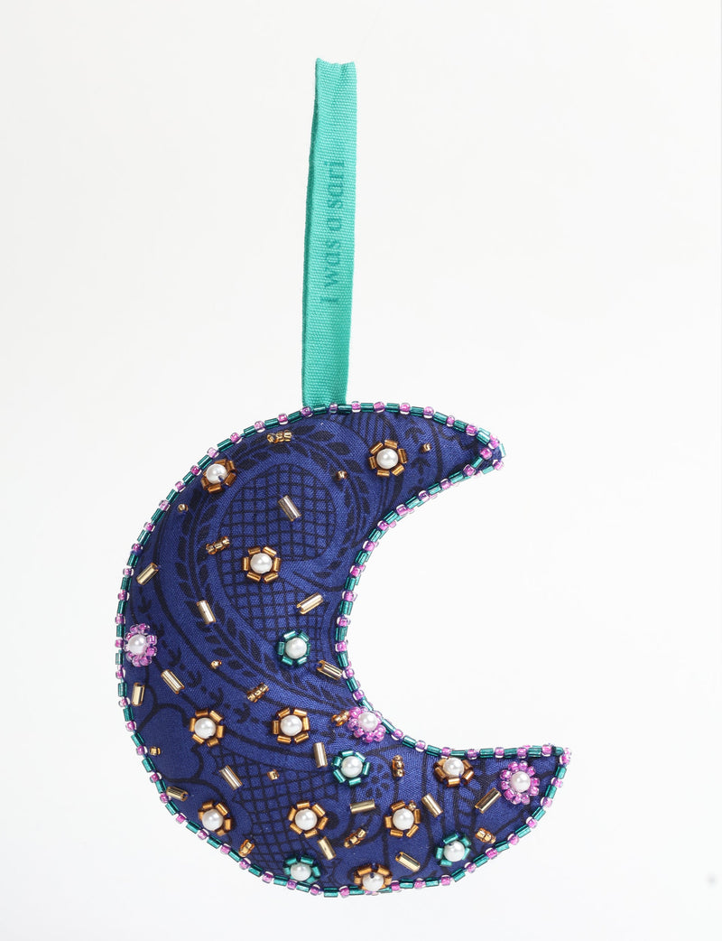 Blue fabric crescent moon ornament with paisley pattern, decorated with multicolored beads and pearls, hanging by a teal