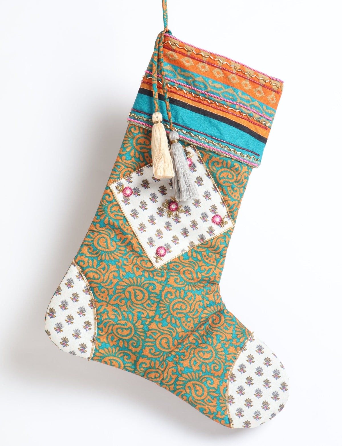 Blue and orange paisley Christmas stocking with white floral patch and two hanging tassels, front view on white background