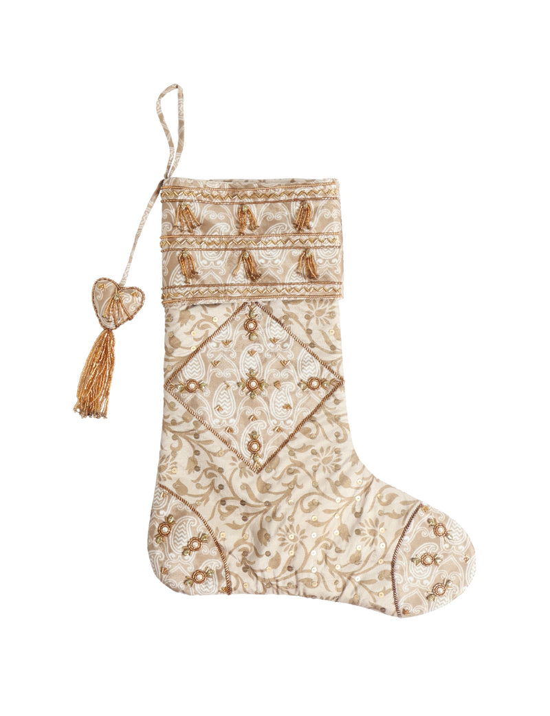 Beige patchwork Christmas stocking with leaf and swirl patterns, gold bead tassels, and heart-shaped hanging loop detail