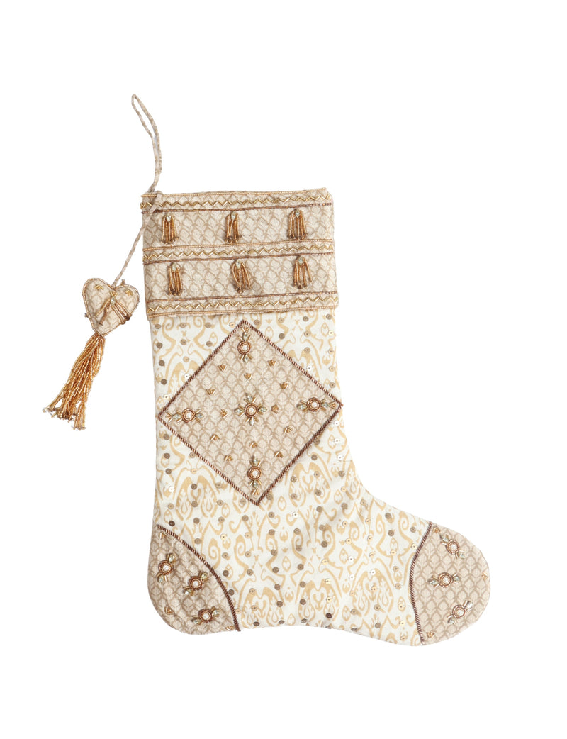 Beige patchwork Christmas stocking with Indian ethnic patterns, gold bead tassels, and sequin embellishments, hanging view