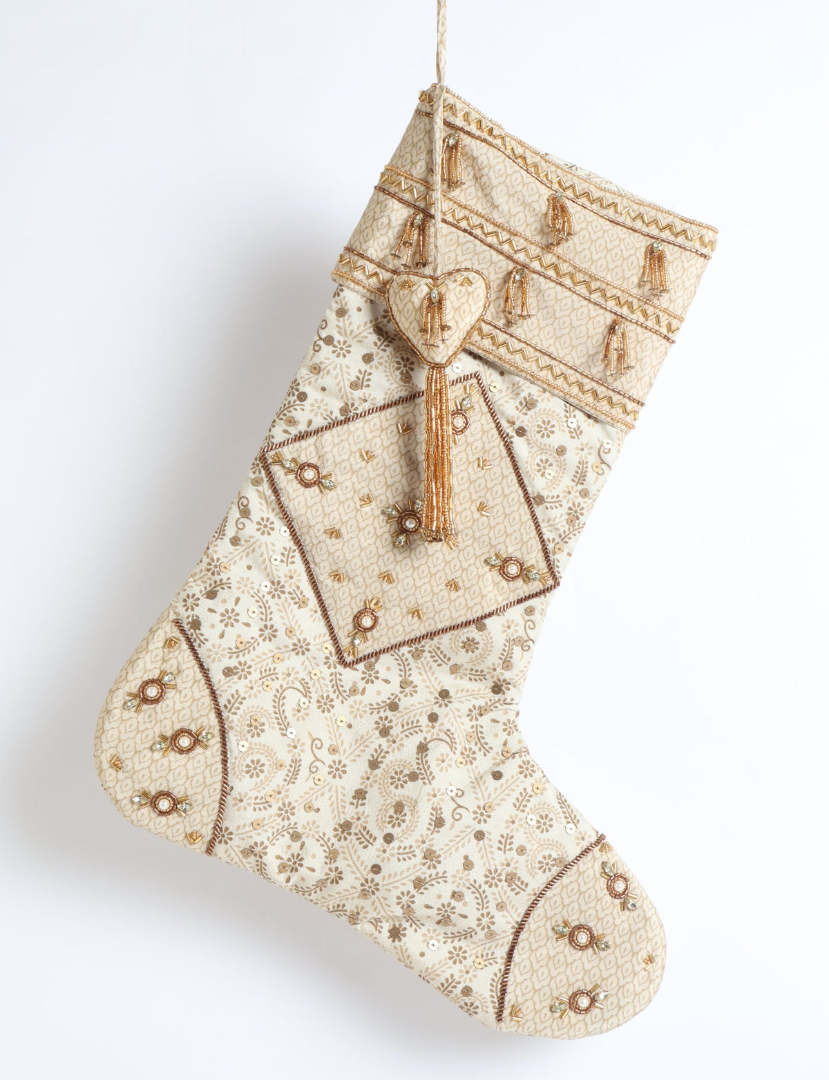Beige patchwork Christmas stocking with leaf patterns and gold bead tassel embellishments hanging against white background