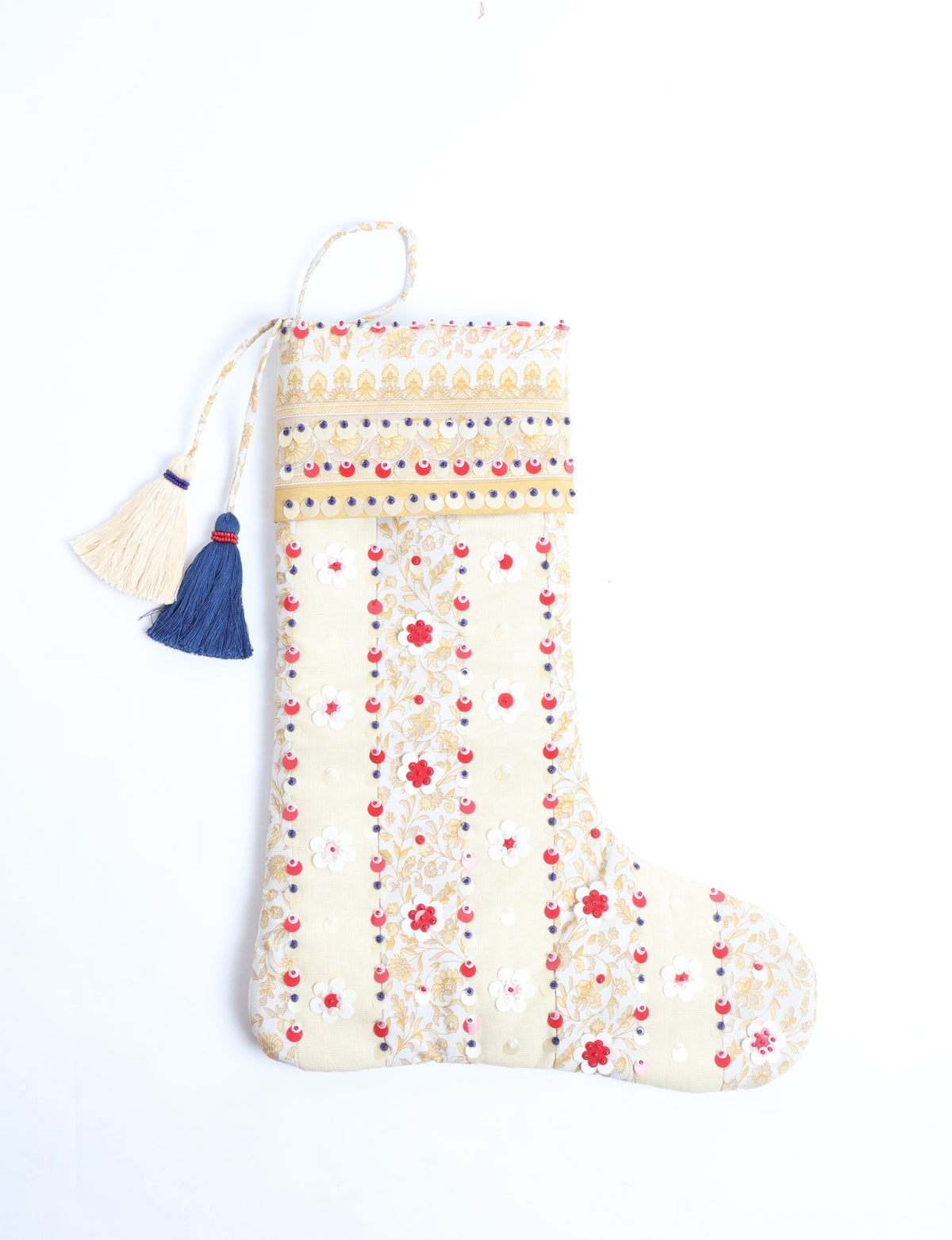 Cream Christmas stocking with gold floral print, red and white sequin flowers, and blue and cream tassels hanging flat