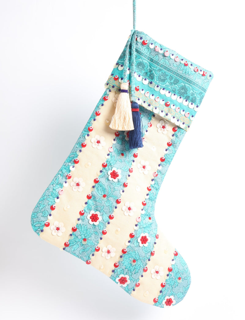 Christmas stocking with turquoise floral pattern, cream stripes, red and white sequins, and two hanging tassels, flat lay view