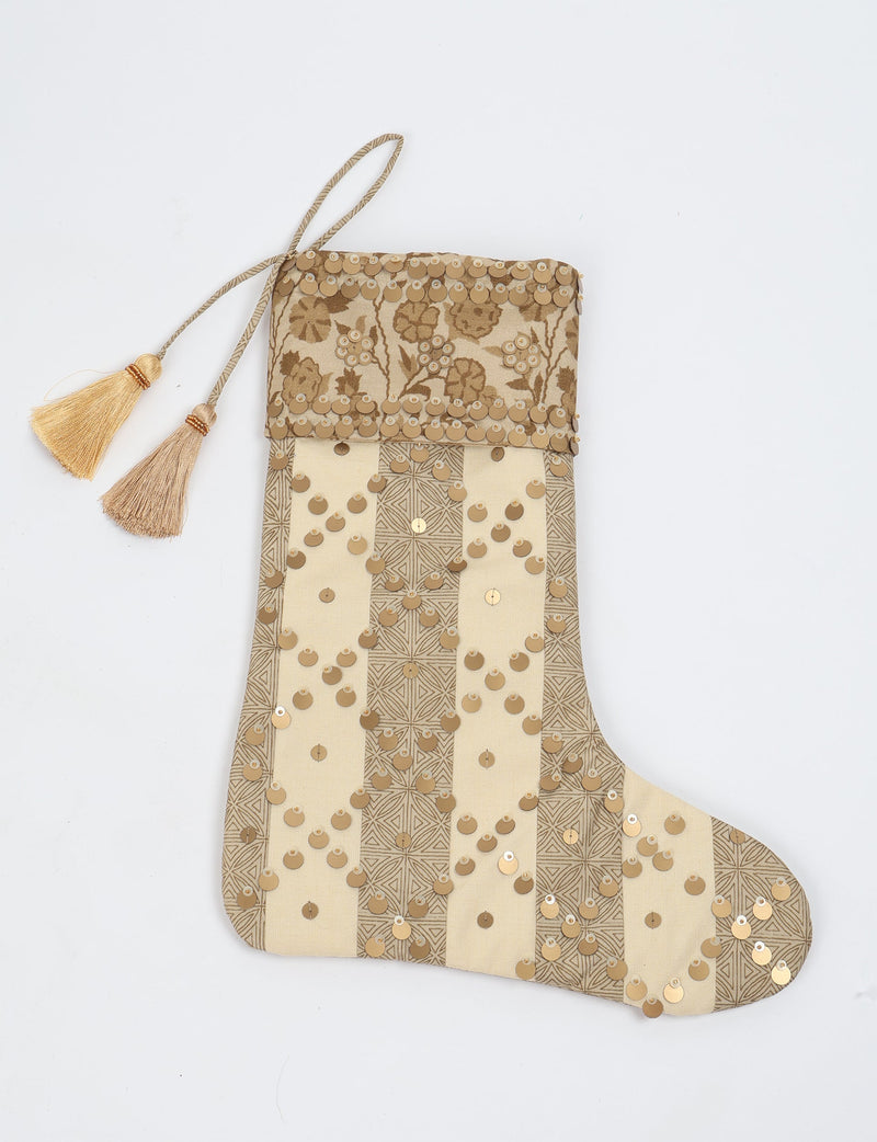 Beige and tan striped Christmas stocking with floral pattern, gold sequins, and two tassels on hanging loop, flat lay view