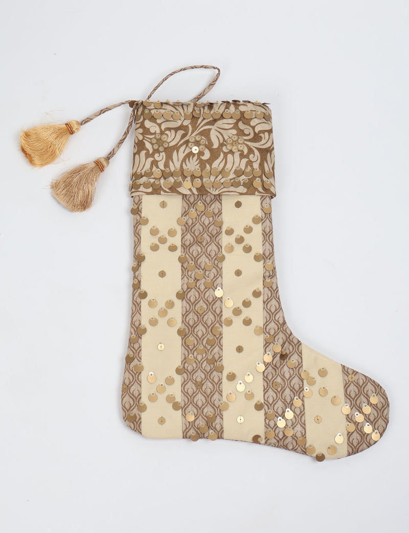 Beige and brown striped Christmas stocking with floral pattern, gold sequins, and two gold tassels on hanging loop, flat lay