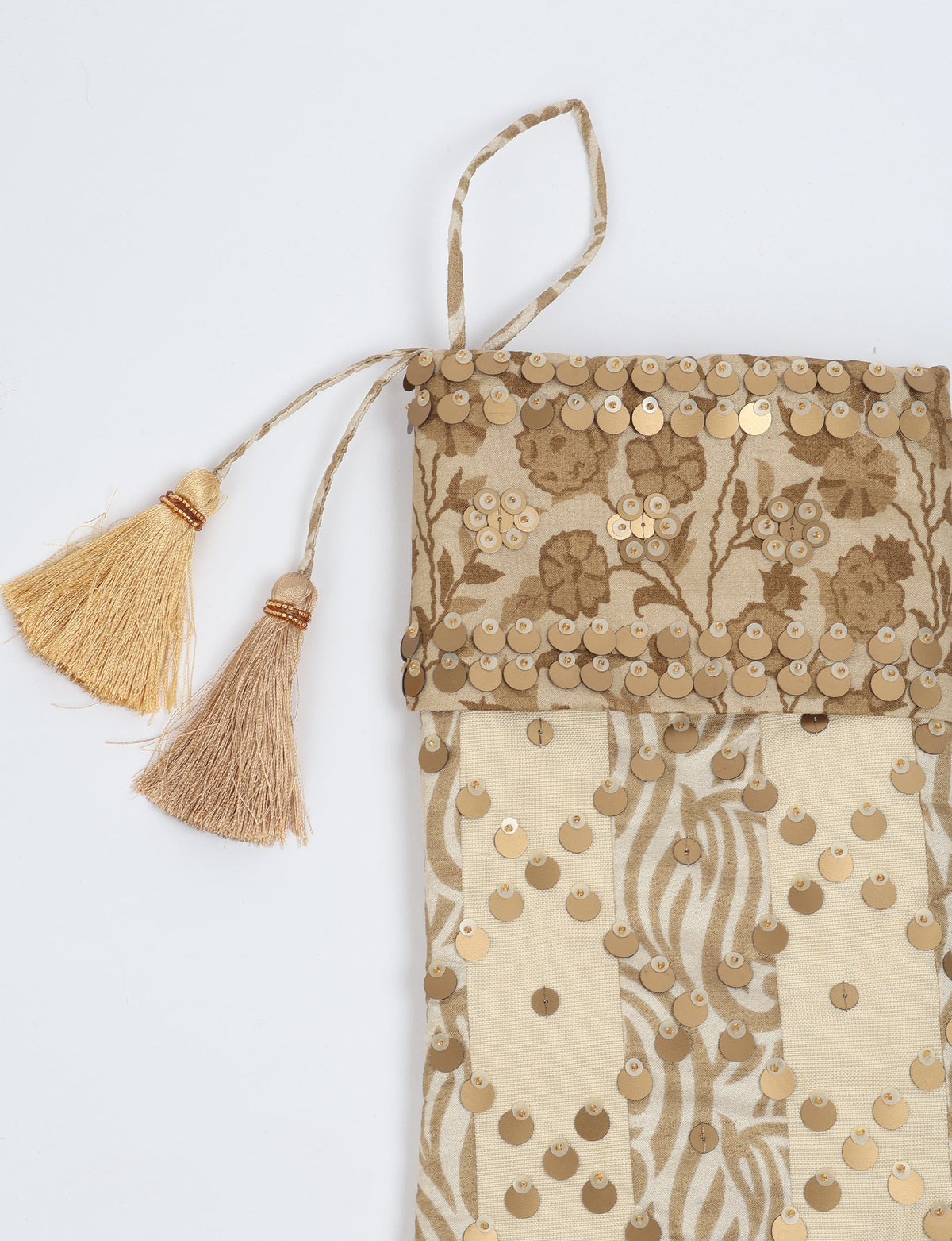 Beige and tan striped Christmas stocking with floral pattern, gold sequins, and two hanging tassels, flat lay view