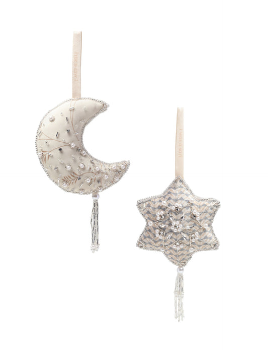 Set of two handcrafted silver ornaments — crescent moon and snowflake — made from recycled sari fabric and filled with organic cotton. Detailed with pearls, sequins, and glass beads. A festive example of upcycled clothing, eco clothing, natural clothing, recycled material clothing, products made from textile waste, repurposed clothing, carbon neutral fashion, and environment friendly clothing.