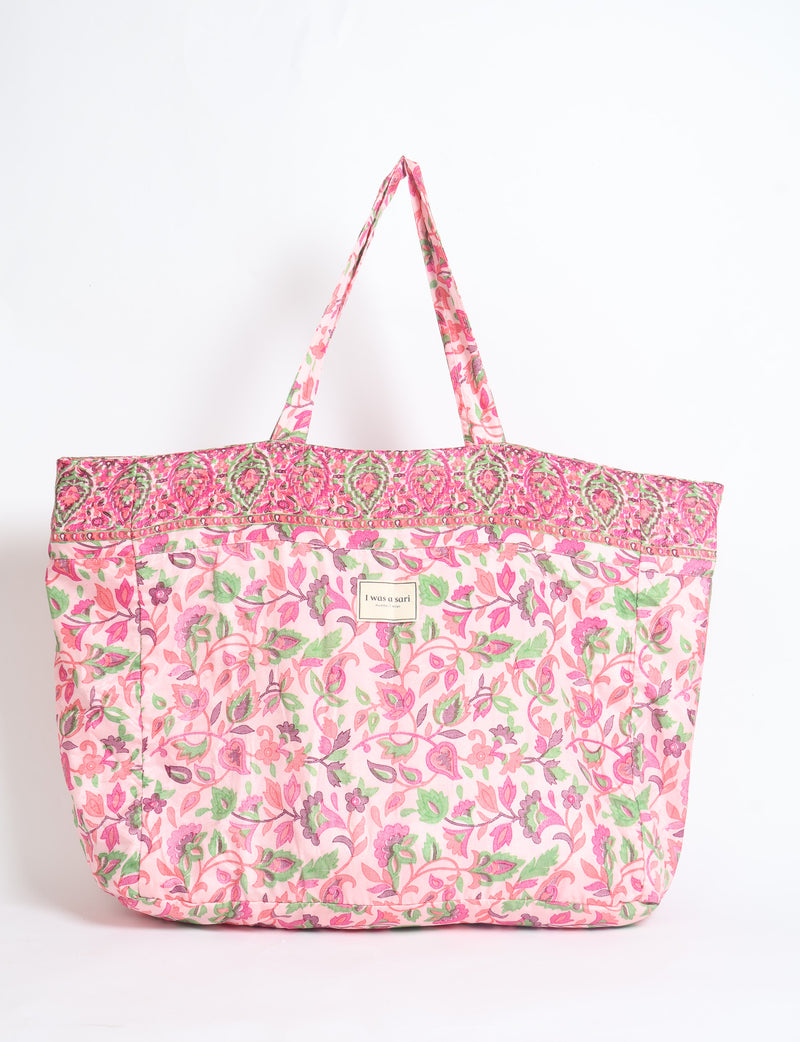 Pink tropical floral patterned fabric beach bag with two handles and "I was a sari" label on front, front view