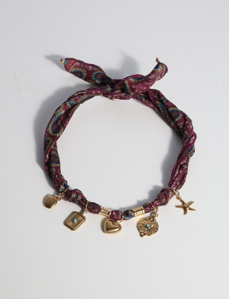 Red tropical patterned bandana necklace with gold-tone charms including a heart, starfish, and turquoise accents, flat lay view