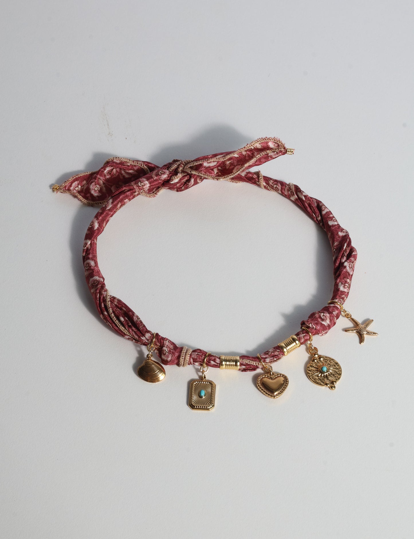Bandana necklace with gold-plated charms, adjustable tie-back design, stainless steel hardware, handmade statement necklace, sustainable fashion accessory.
