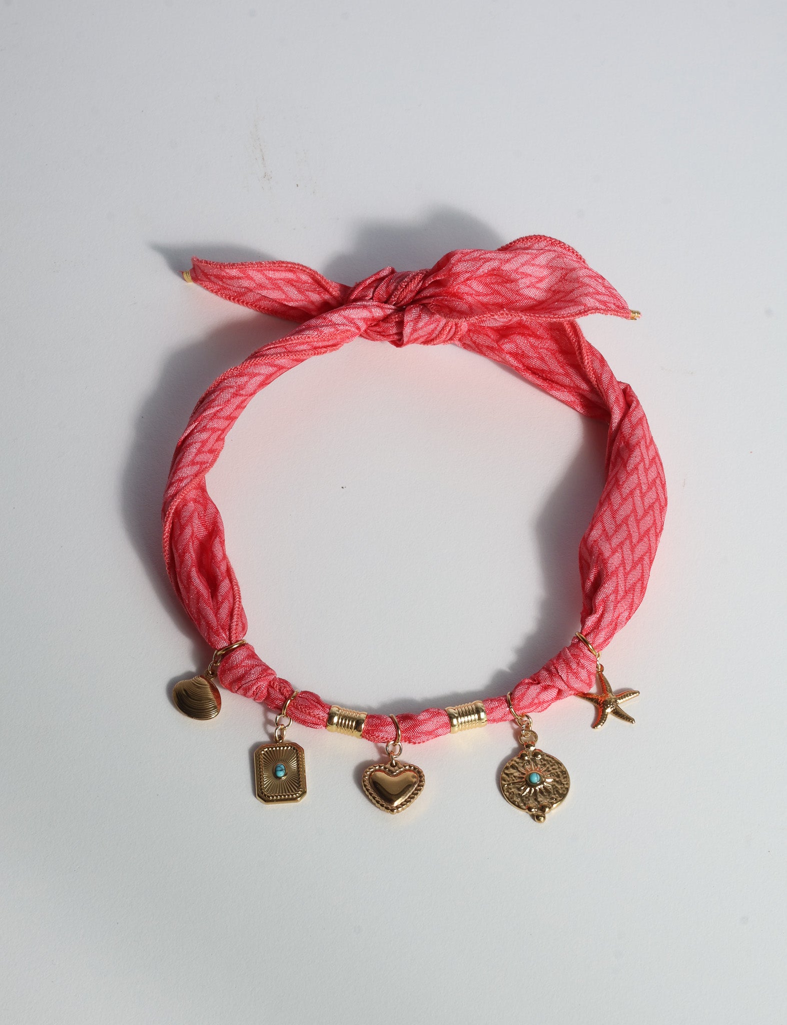 Pink geometric patterned bandana necklace with gold-tone charms including heart, starfish, and turquoise accents, flat lay view