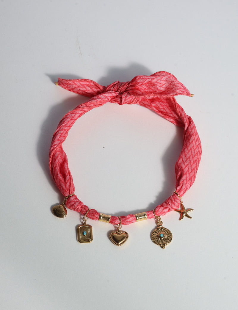 Pink geometric patterned bandana necklace with gold-tone charms including heart, starfish, and turquoise accents, flat lay view