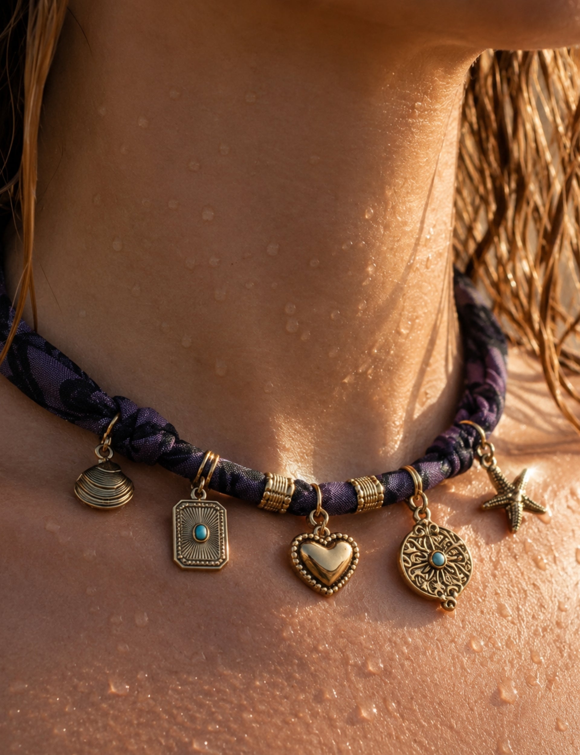 Purple bandana necklace with gold-tone charms including heart, starfish, and turquoise-accented pendants, worn on neck