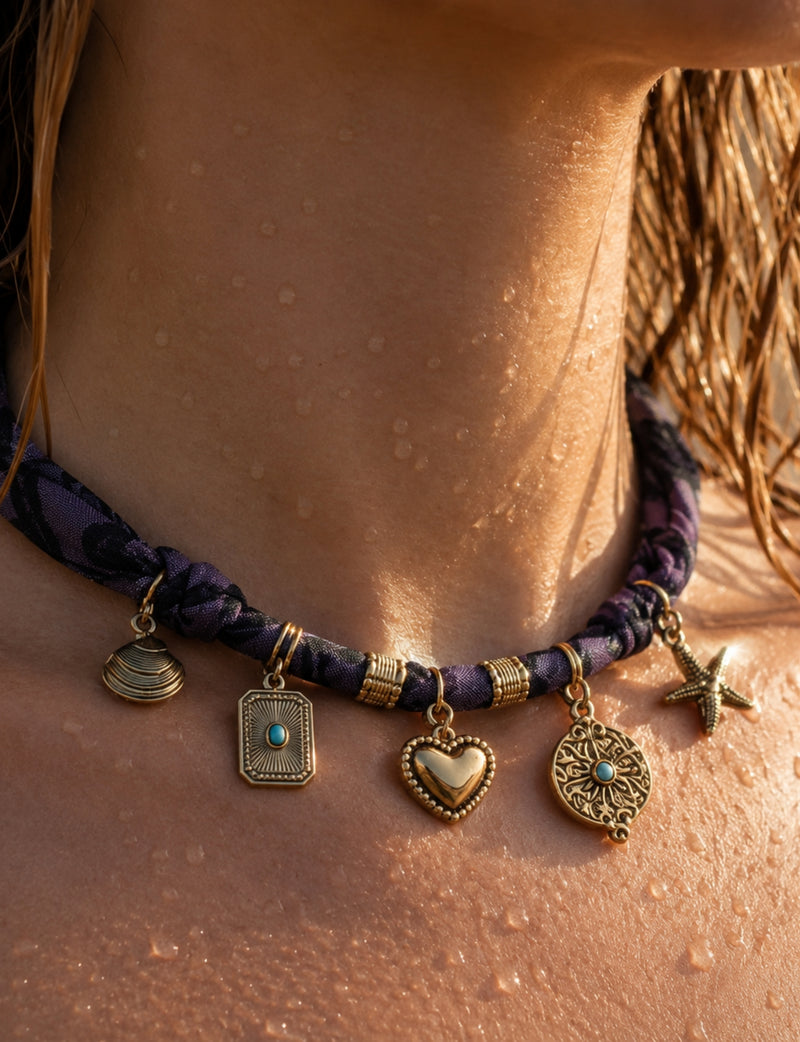 Purple bandana necklace with gold-tone charms including heart, starfish, and turquoise-accented pendants, worn on neck