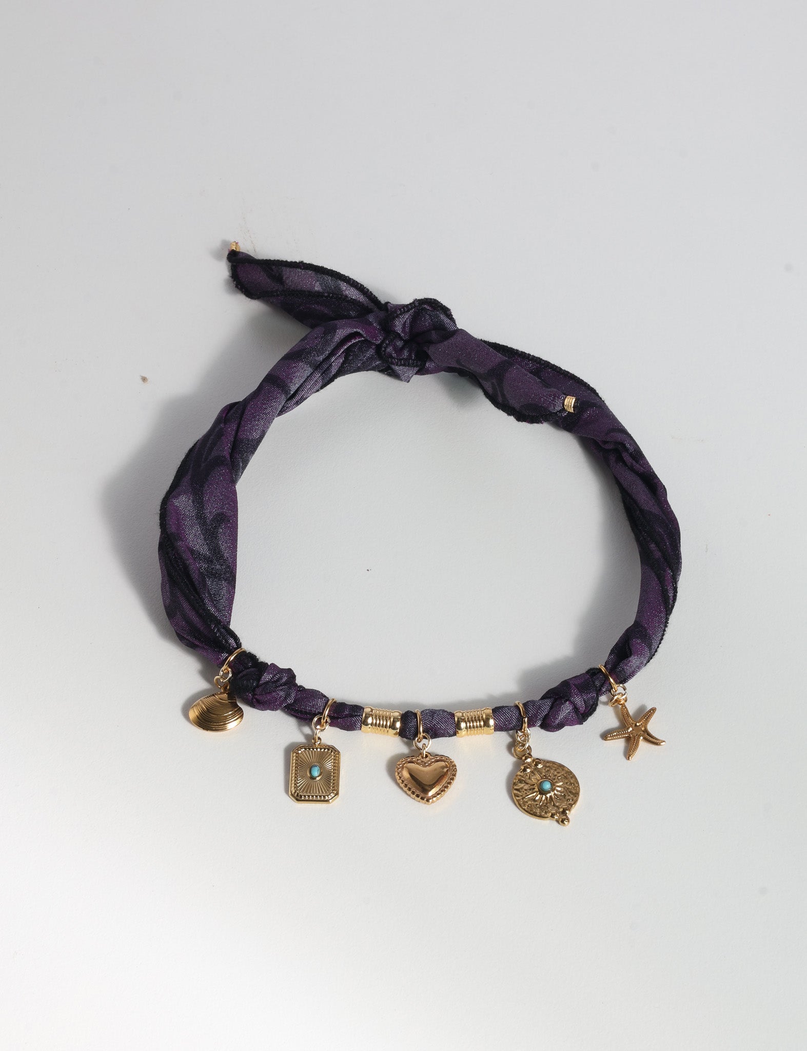Purple abstract patterned bandana necklace with gold-tone charms including heart, starfish, and turquoise accents, flat lay view