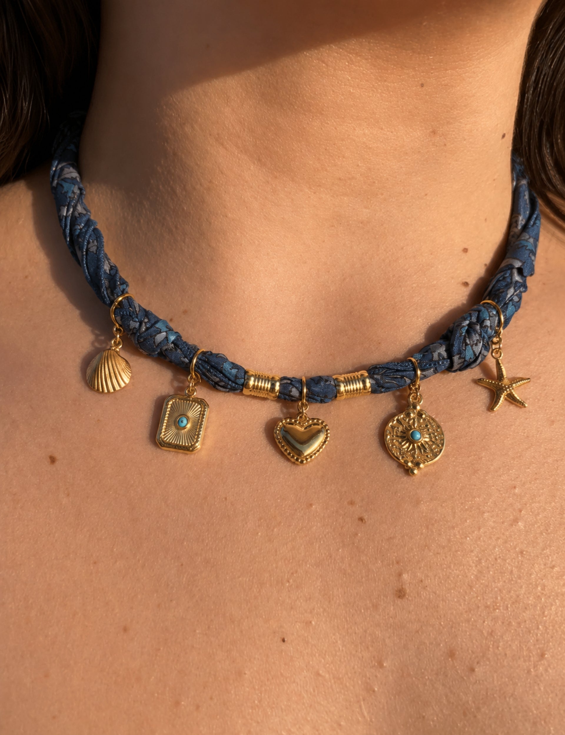 Grey tropical patterned bandana necklace worn on neck with gold shell, heart, starfish, and decorative charms hanging