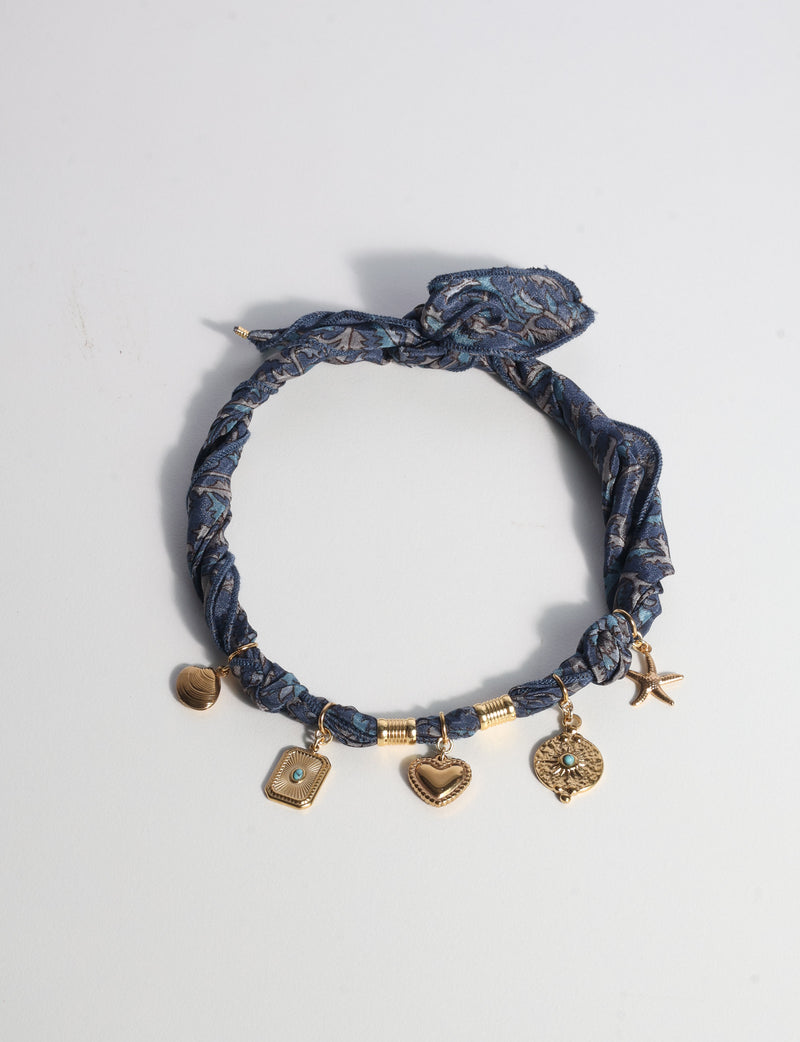 Grey tropical patterned bandana necklace with gold-tone charms including heart, starfish, and shell, flat lay on white background