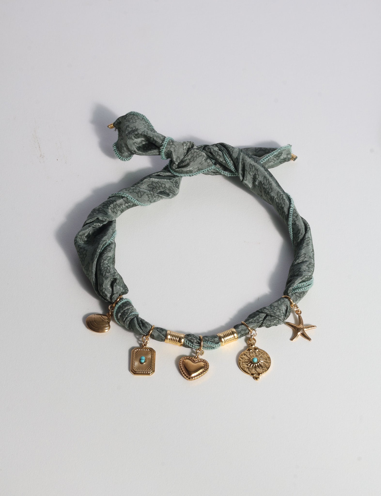 Green tropical patterned bandana necklace with gold-tone charms including heart, starfish, and shell, flat lay view