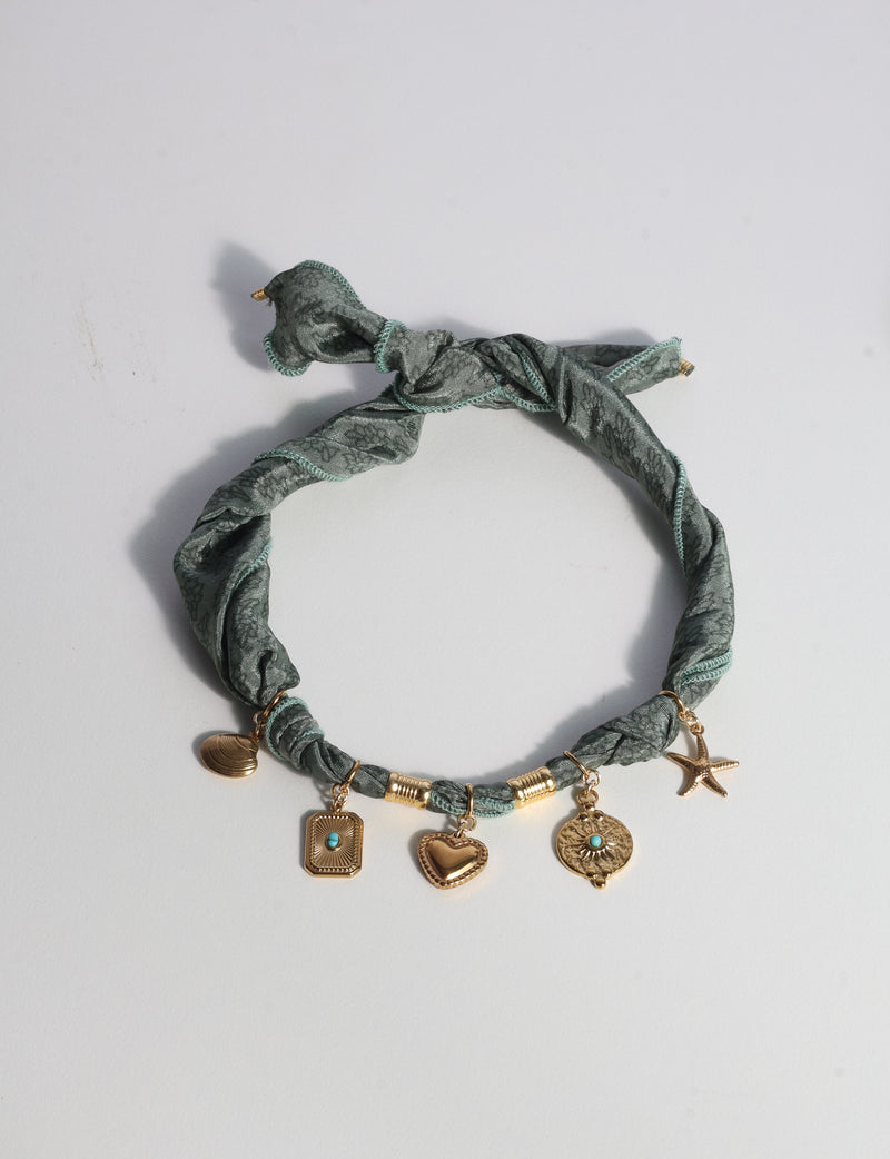 Green tropical patterned bandana necklace with gold-tone charms including heart, starfish, and shell, flat lay view