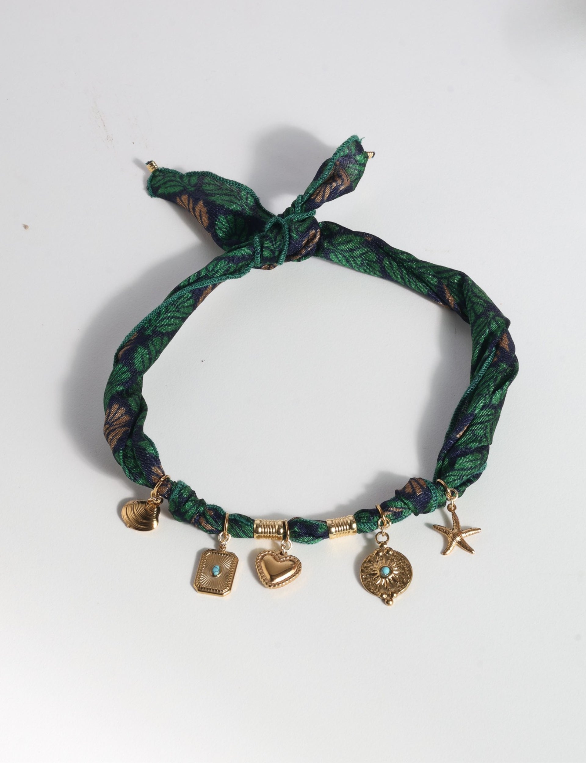 Green floral fabric bandana necklace with gold-tone charms including heart, starfish, and shell, flat lay on white background