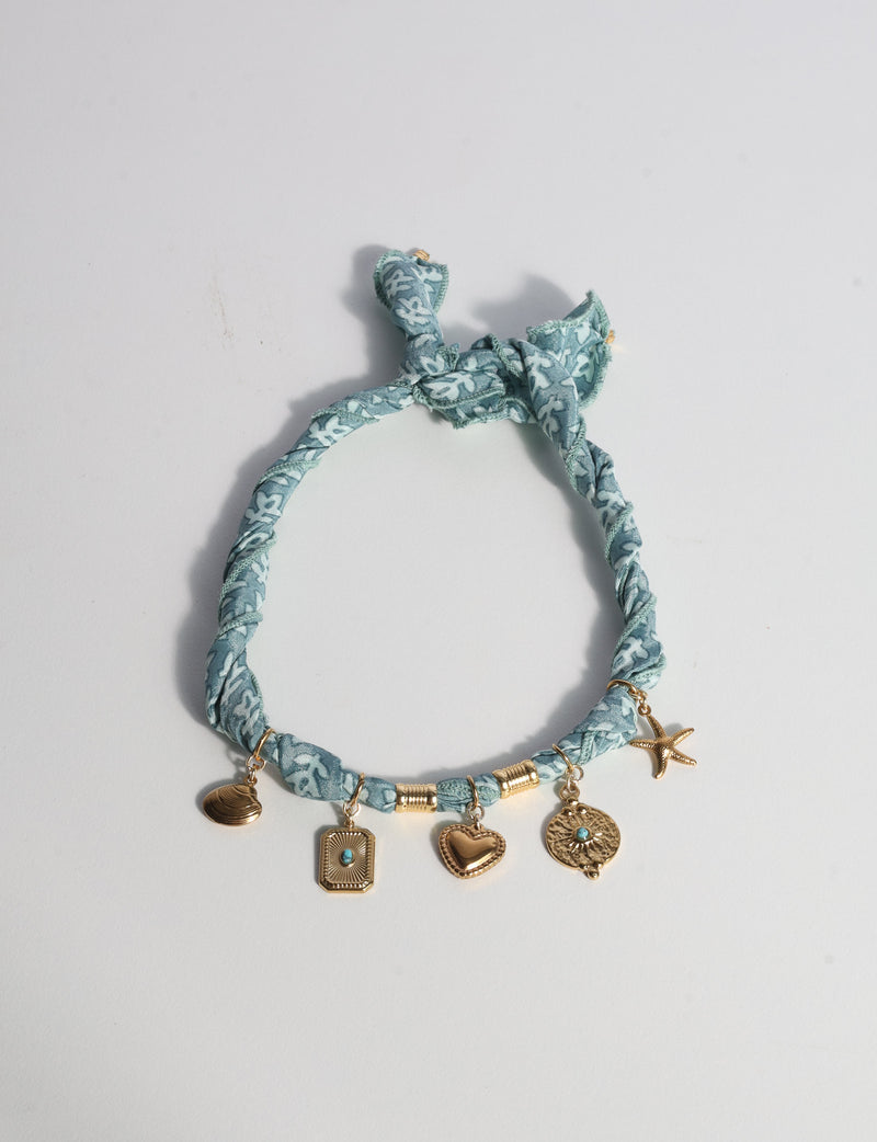 Grey bandana necklace with white leaf pattern and five gold-tone charms including heart, starfish, and shell, flat lay view