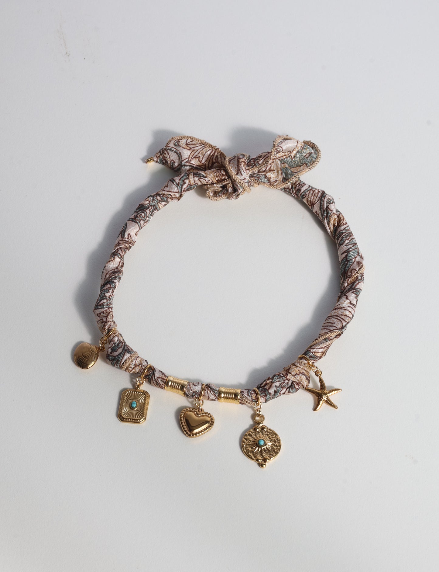 Bandana necklace with gold-plated charms, adjustable tie-back design, stainless steel hardware, handmade statement necklace, sustainable fashion accessory.