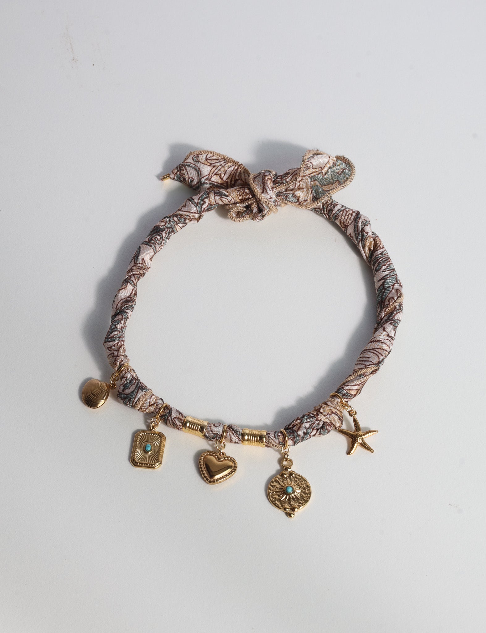Beige tropical patterned bandana necklace with gold-tone charms including heart, starfish, and turquoise accents, flat lay view