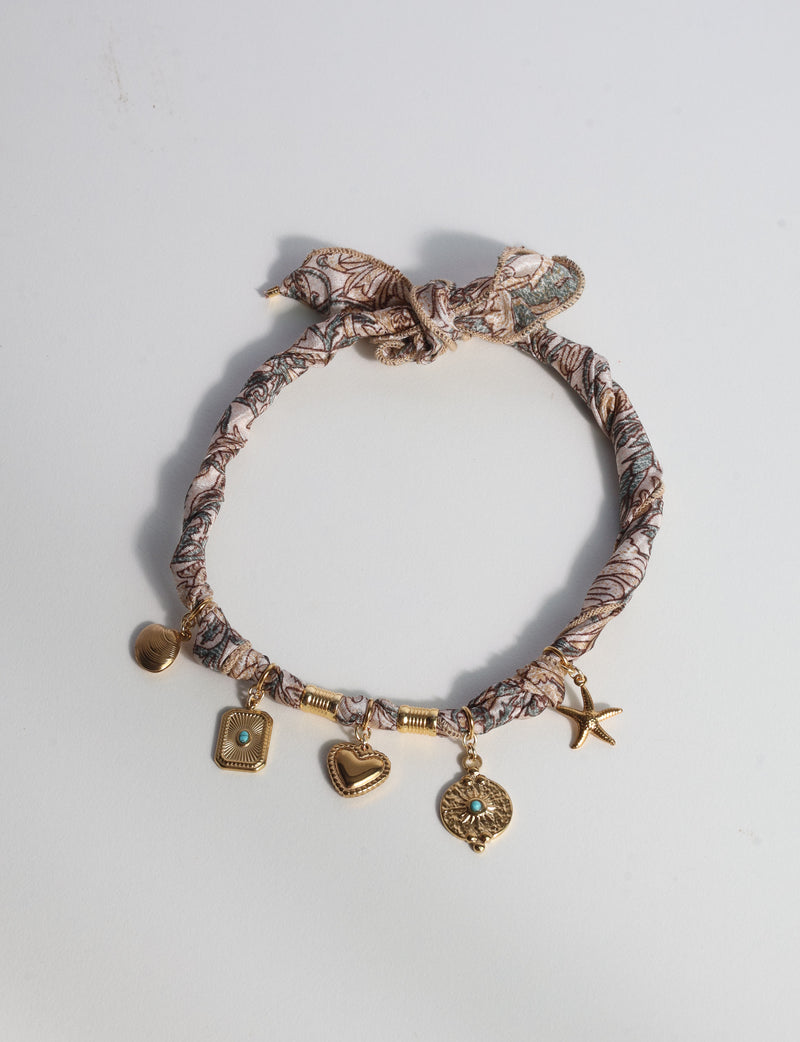 Beige tropical patterned bandana necklace with gold-tone charms including heart, starfish, and turquoise accents, flat lay view