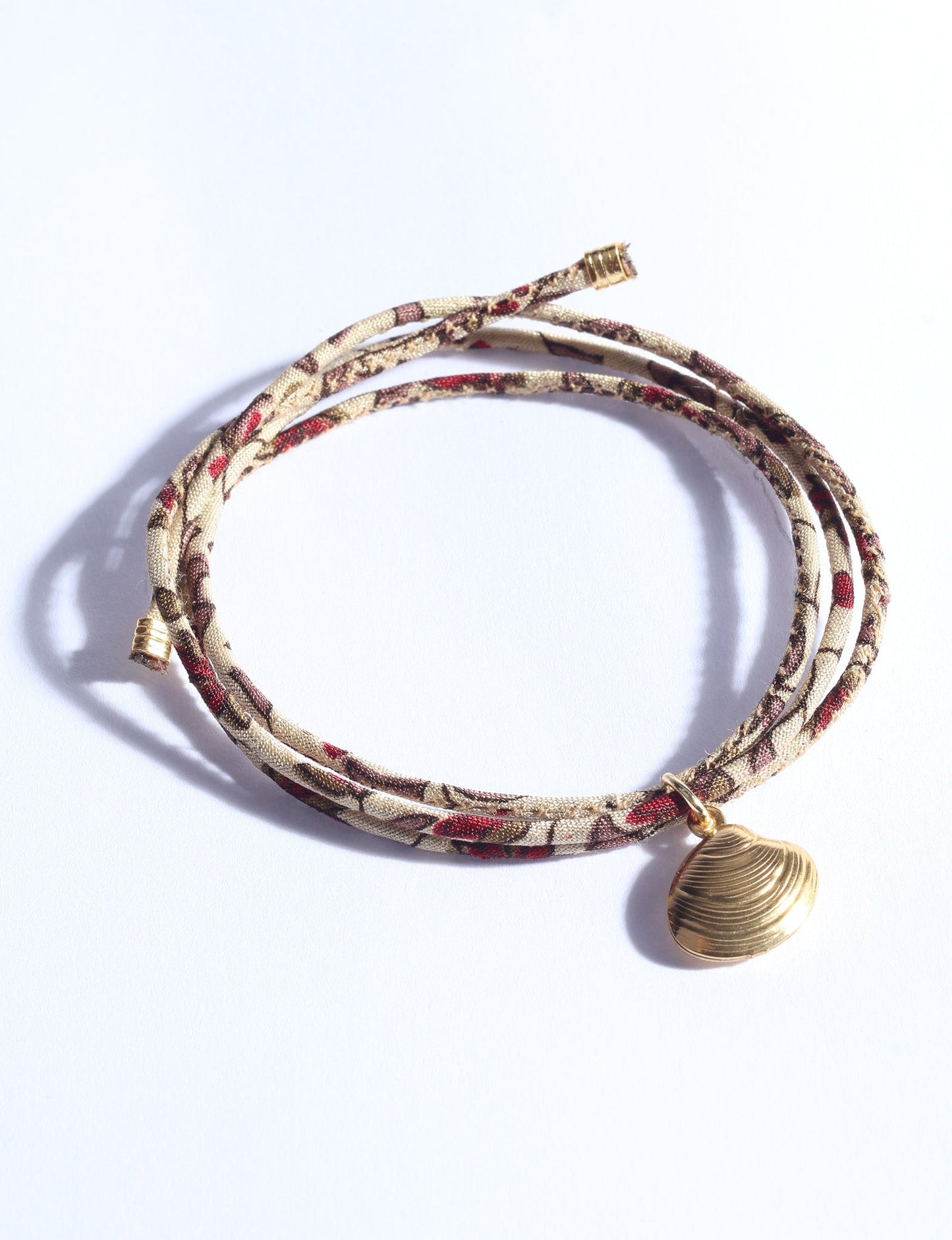 Adjustable slim cord bracelet with gold-plated stainless steel shell charm inspired by upcycled women’s clothing, sustainable women’s clothing, eco friendly clothes, recycled sustainable fashion, carbon neutral clothing, and environment friendly clothing values.