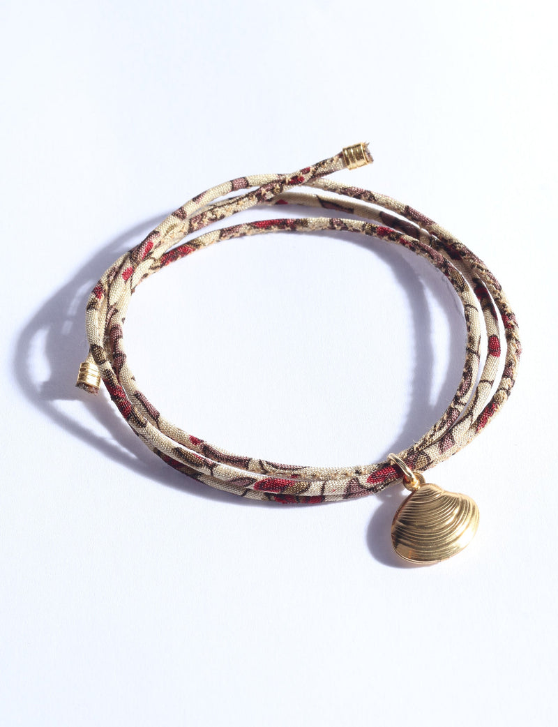 Beige abstract patterned cord bracelet with gold-tone shell charm, shown coiled on white background, front view