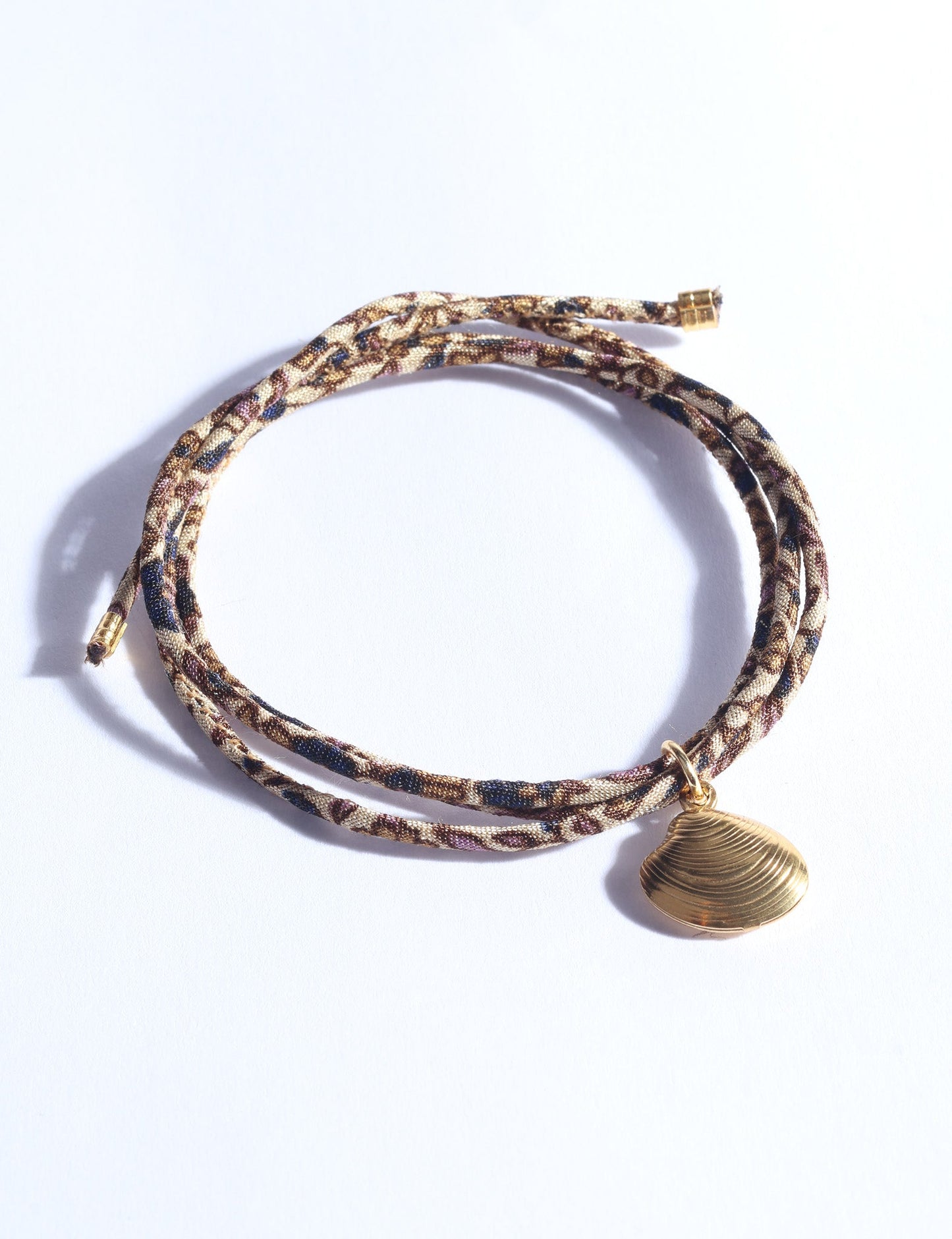 Adjustable slim cord bracelet with gold-plated stainless steel shell charm inspired by upcycled women’s clothing, sustainable women’s clothing, eco friendly clothes, recycled sustainable fashion, carbon neutral clothing, and environment friendly clothing values.