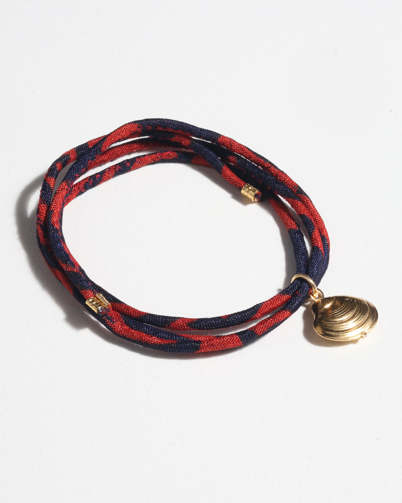 Blue and red abstract patterned cord bracelet with gold-tone shell charm, shown coiled on white background