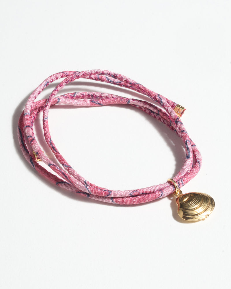 Pink abstract patterned cord bracelet with gold-tone shell charm, shown coiled on white background