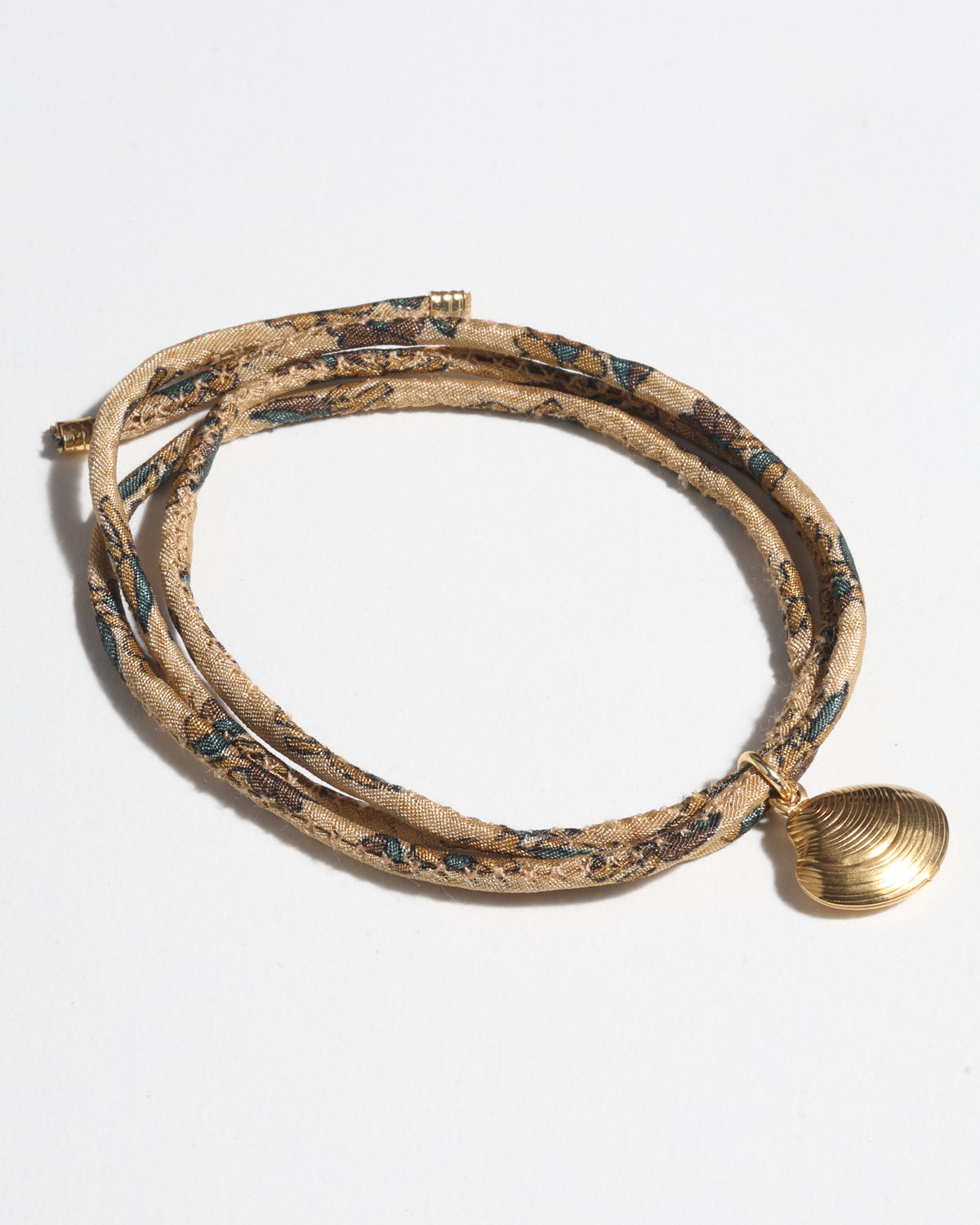 Beige tropical patterned cord bracelet with gold-tone shell charm, shown coiled on white background