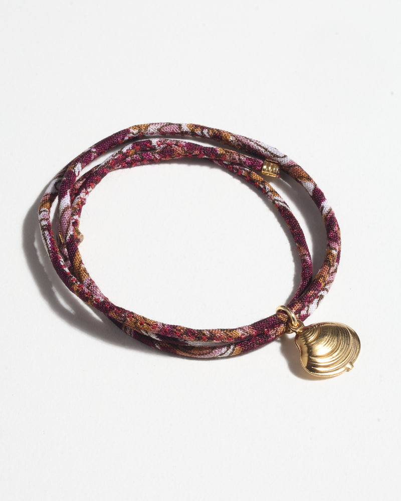 Red tropical patterned cord bracelet with a gold-tone shell charm, shown coiled on a white background