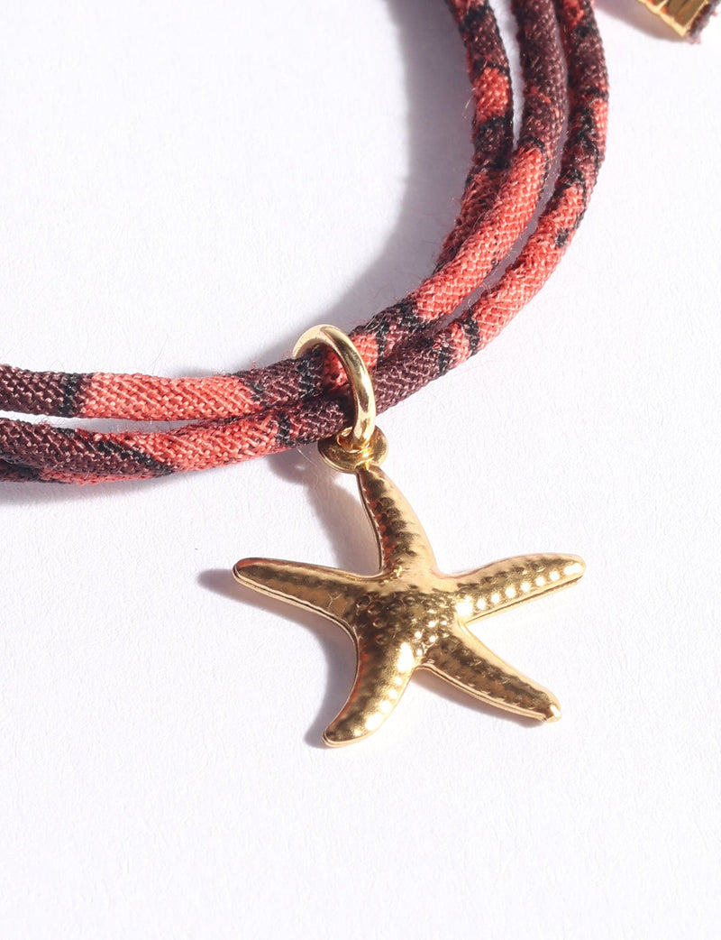 Red and brown patterned cord bracelet with gold-tone starfish charm, close-up flat lay on white background