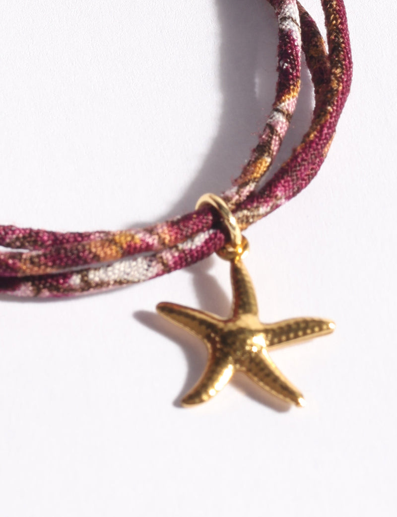 Cord bracelet in burgundy, pink, and brown tones with a gold starfish charm, shown in close-up on white background