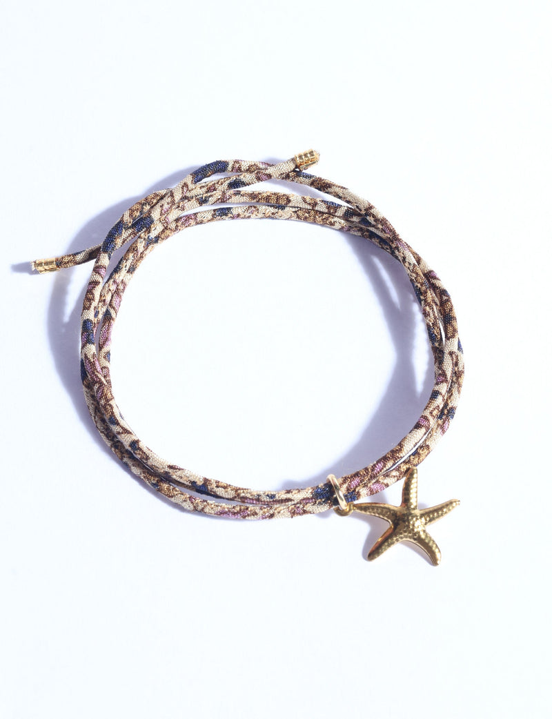 Braided cord bracelet with gold starfish charm, multicolor pattern with beige, brown, blue, and purple tones, flat lay view