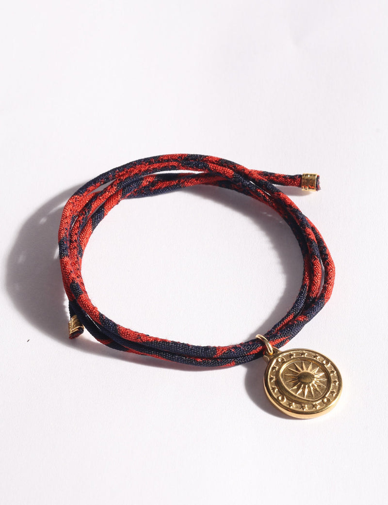 Blue and red abstract patterned cord bracelet with a round gold sun medallion charm, shown flat on white background