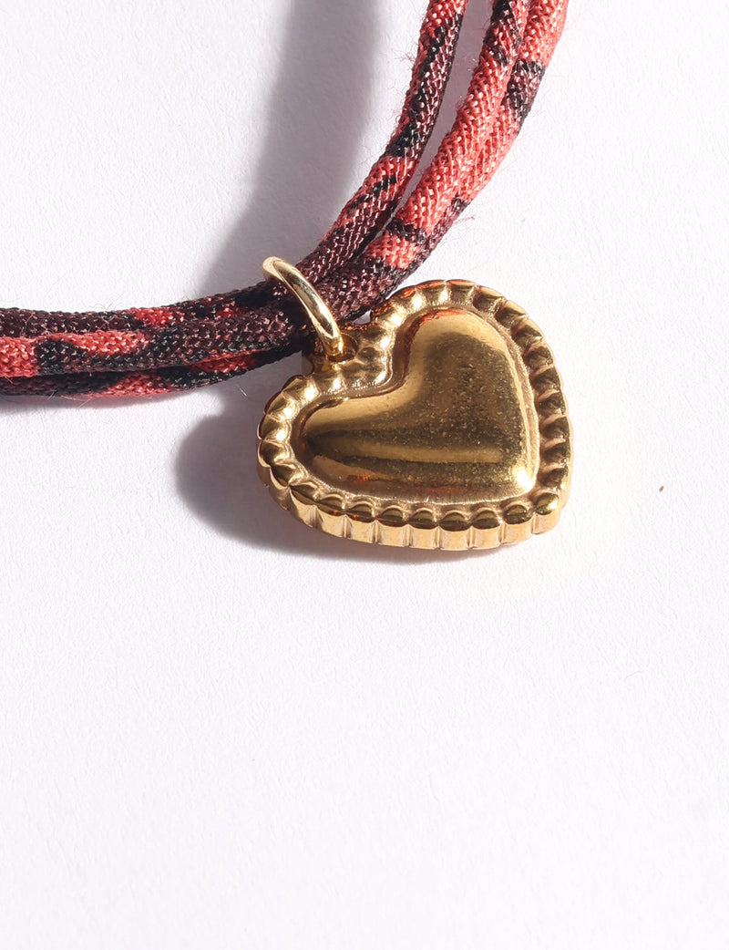 Brown and dark red abstract patterned cord bracelet with a gold-tone heart-shaped charm, close-up view on white background
